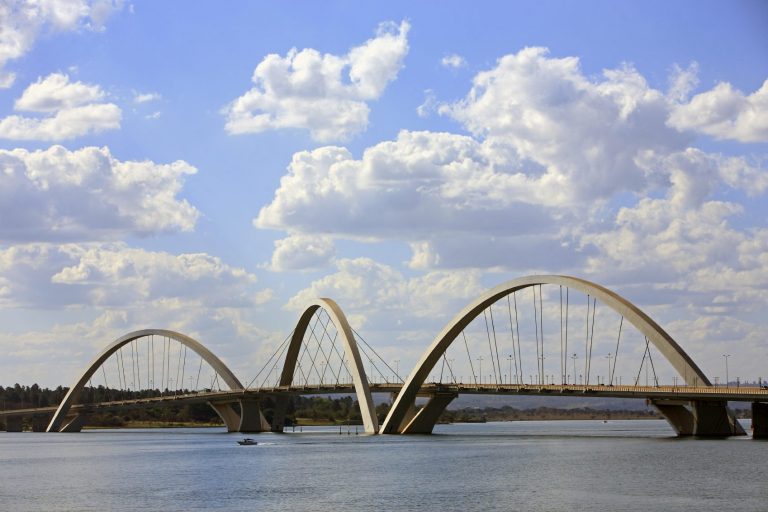 Helle Brücke mit mehreren Bögen über einem Gewässer unter bewölktem Himmel.