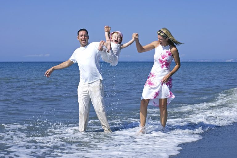 Familie am Strand, Eltern halten ein glückliches Kind in der Luft vor dem Wasser.