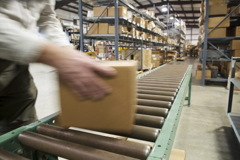 Hand legt ein Paket auf ein Förderband in einem Lagerhaus.