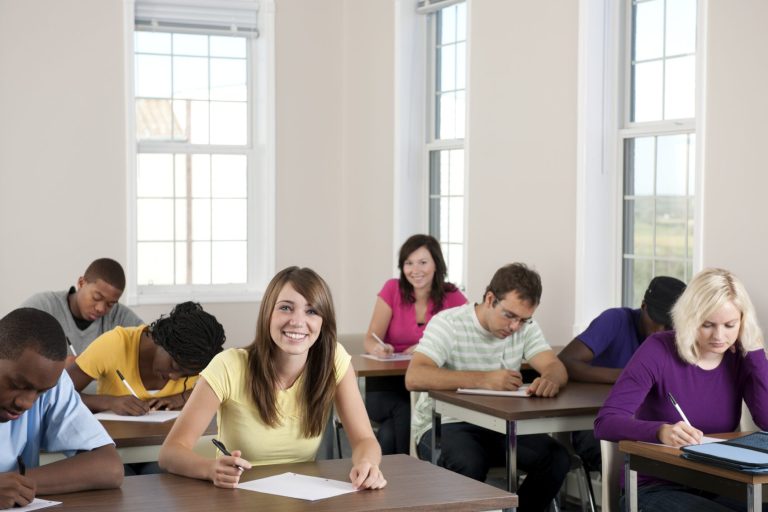 Gruppe von Schülern, die in einem Klassenzimmer Prüfungen schreiben, einige lächeln.