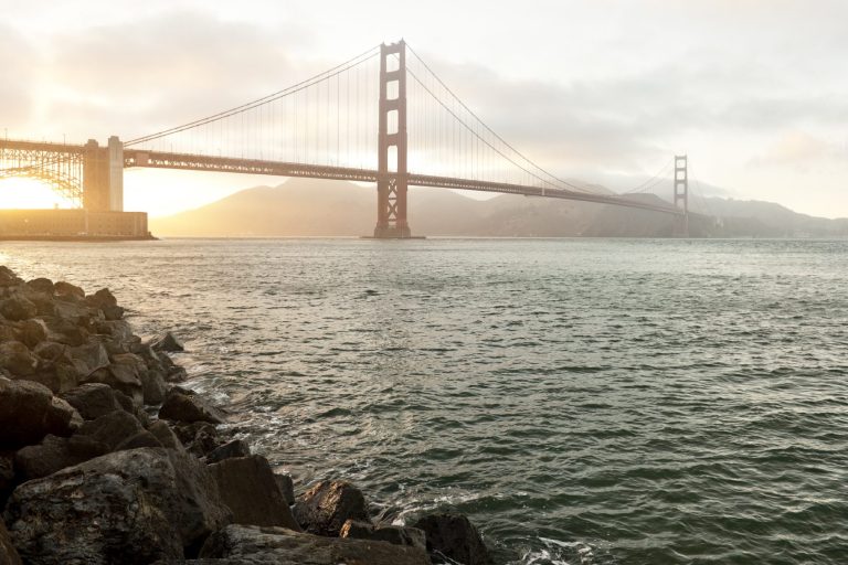 Goldene Gate Bridge bei Sonnenaufgang, umgeben von Nebel und Wasser.