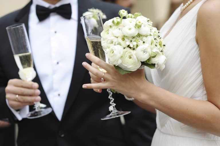 Hochzeitsfeier mit Braut in elegantem Kleid und Blumenstrauß, Sektgläser in der Hand.