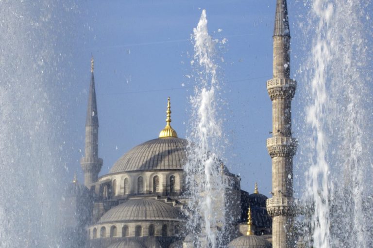 Die Silhouette einer Moschee mit Minaretten und Brunnen im Vordergrund.