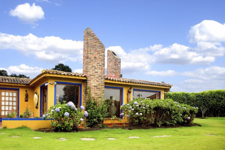 Farbige Landhausfassade mit Blumen und blauem Himmel im Hintergrund.