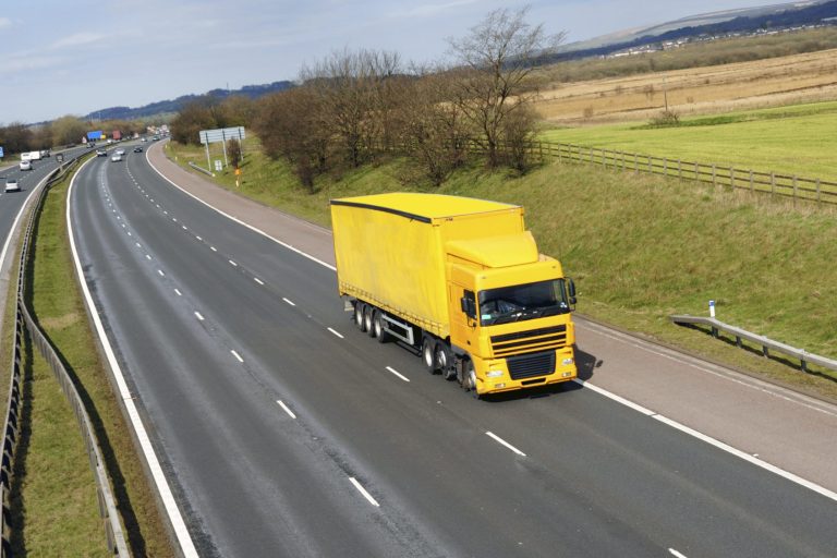 Gelber Lkw fährt auf einer Autobahn mit Freiflächen im Hintergrund.